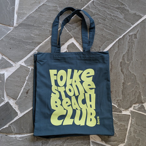 Teal tote bag with acid yellow text on a stone surface