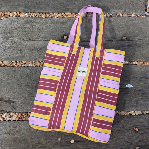Striped pink tote bag with maroon and yellow pattern on a wooden surface