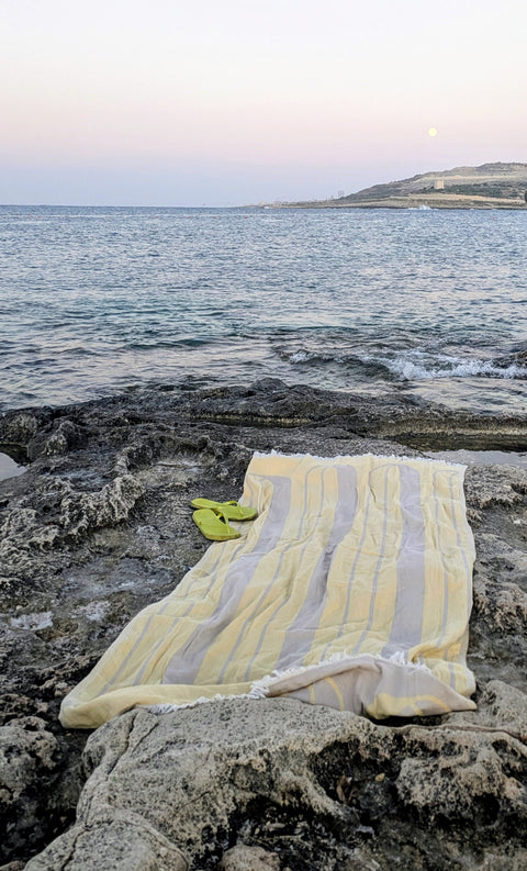 Laes Bridge Turkish Towel - Beach Towel - yellow and beige - laid out on the rocks by the sea - shop now