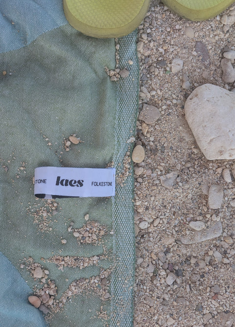 Laes Harbour Turkish Towel - Beach Towel - close up of green/blue towel with logo hanging loop on the sand - shop now