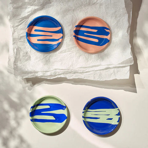 Four round ceramic plates with abstract blue and pink designs on a white surface.