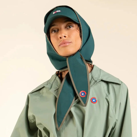 Person wearing a green raincoat and matching headscarf with a visible brand logo on a beige background