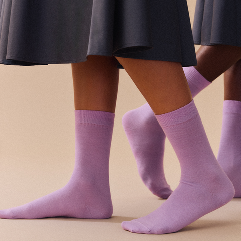 Purple socks worn with a dark skirt on a beige background