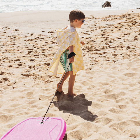 Child with a yellow towel and pink bodyboard on a sandy beach