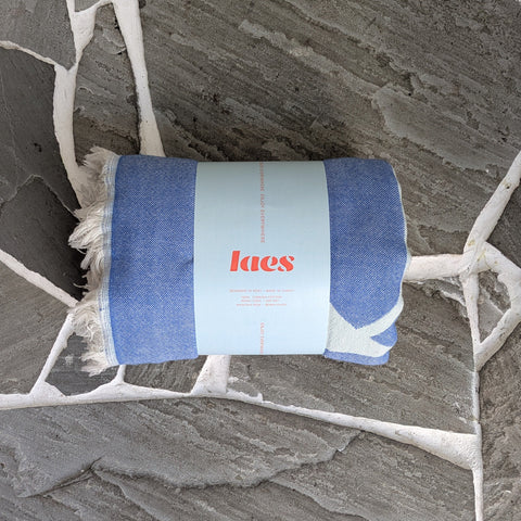 Rolled up blue blanket with 'laes' branding on a stone floor