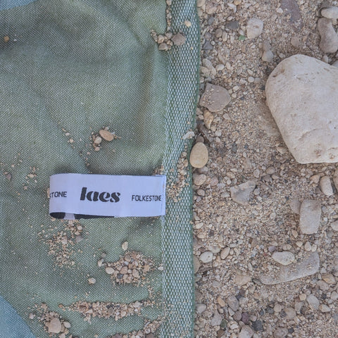 Laes Harbour Turkish Towel - Beach Towel - close up of green/blue towel with logo hanging loop on the sand - shop now