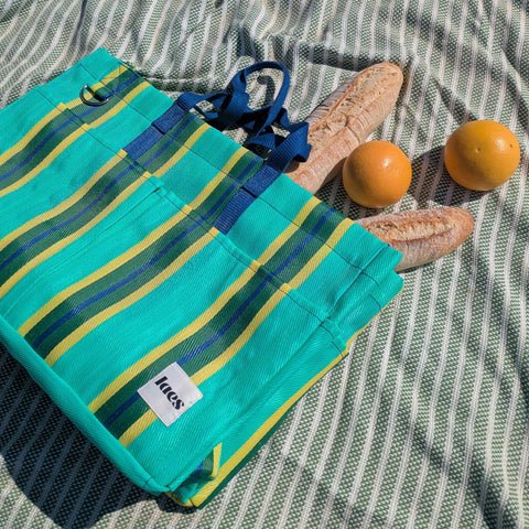 Teal striped bag on a blanket with oranges and a baguette