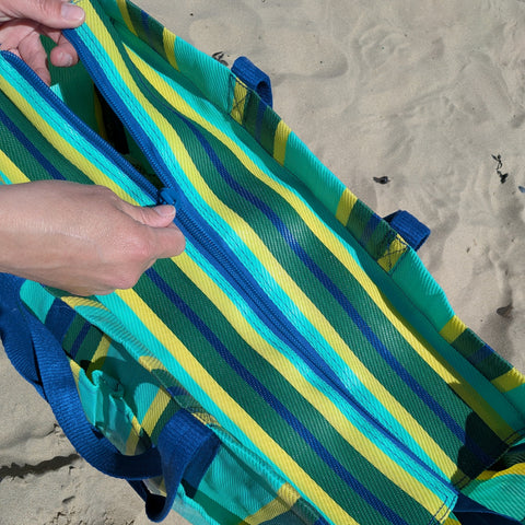 Two hands zipping up a striped bag on a sandy beach
