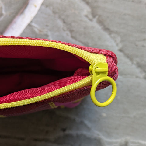 Red pouch with yellow zipper on a textured gray surface