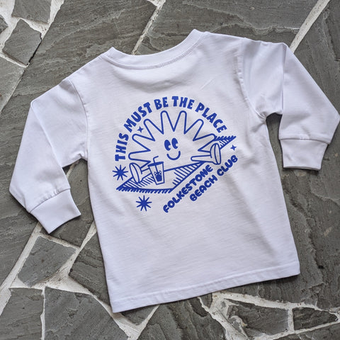White long-sleeve shirt with blue graphic design on a stone surface