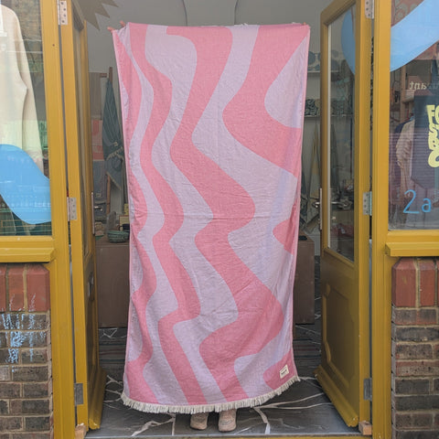Pink and white patterned towel hanging on a door with 'laes' branding.