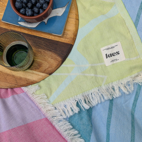 a close up of three towels laid flat together with a wooden tray holding a green glass, a book and a bowl of berries