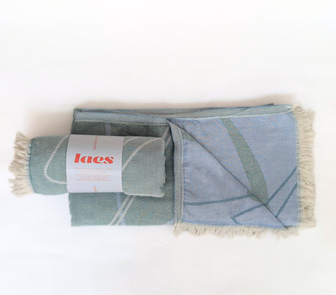 A rolled blue and green patterned towel lying on a folded towel in the same pattern