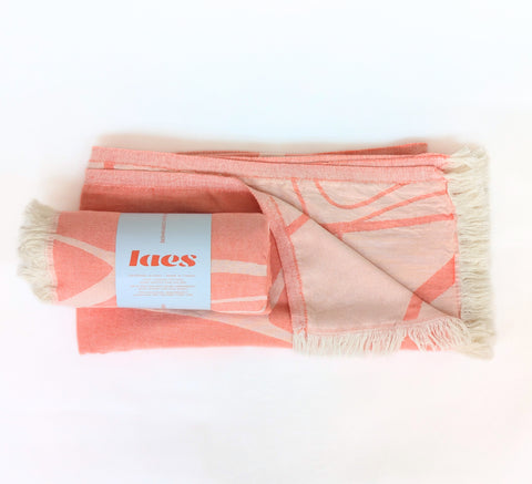 Coral and beige patterned towel with a logo label on a white background