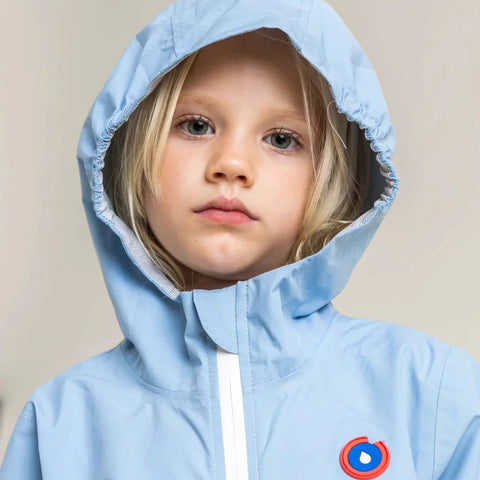 Child wearing a light blue hooded jacket with a logo on a beige background