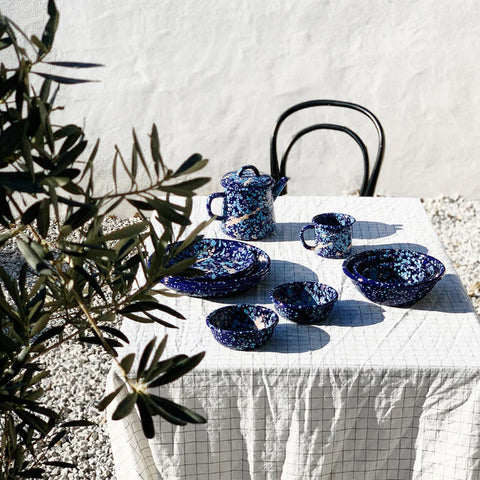 Blue enamel dishes on a white tablecloth with a plant in the background