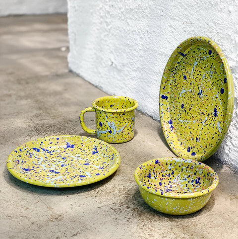 Green enamel tableware set with blue speckles on a concrete surface.