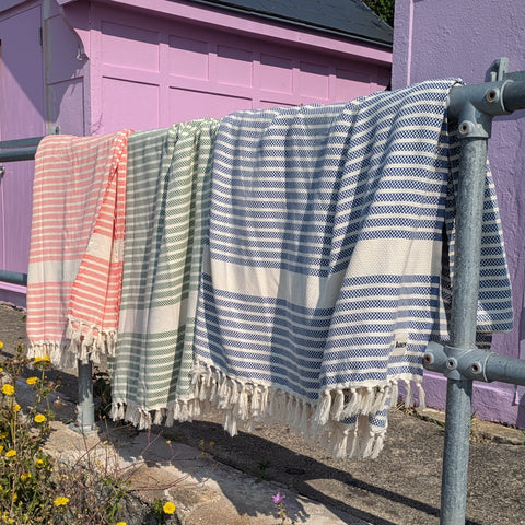 Striped blankets hanging on a metal railing against a pink beach hut