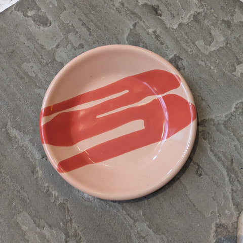 Small coral plate with red design on textured grey tiles