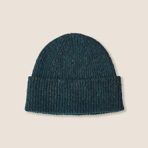 A dark teal ribbed knit beanie hat with subtle multicolor flecks, presented flat against a solid light beige background.