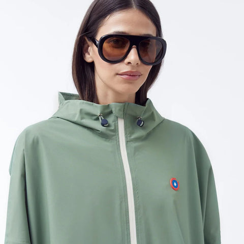Person wearing a green raincoat with a brand logo on a light gray background