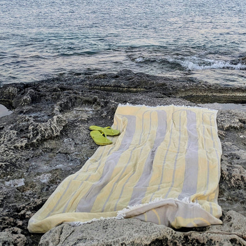 Laes Bridge Turkish Towel  - Beach Towel - yellow and beige - laid out on the rocks by the sea - shop now