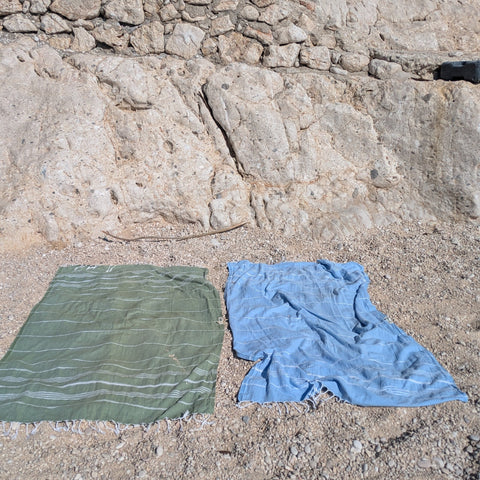 Two towels, one green and one blue, on a rocky beach.