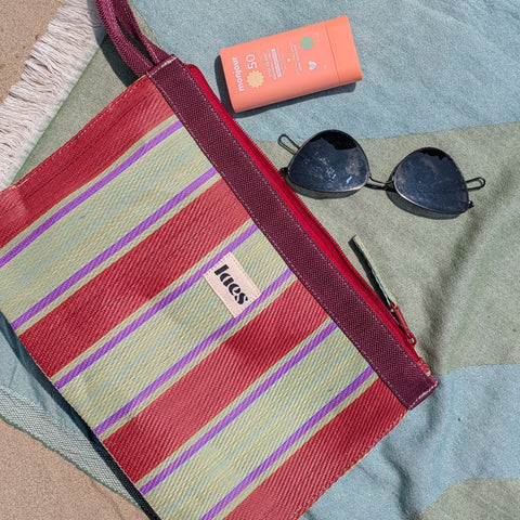 Striped 'laes' branded pouch, sunglasses, and sunscreen on a beach towel