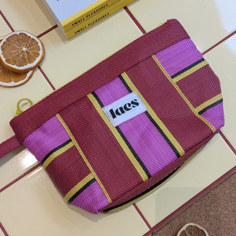 a pink striped pouch lying on a yellow tiled table with orange slices nearby