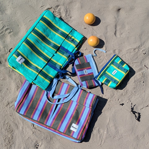 Colorful striped bags on a sandy beach with two oranges.