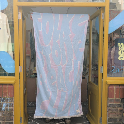 Purple and blue towel with lettered design being held up in a doorway of a yellow shop