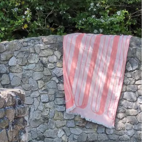 Pink towel patterned with arches hanging on a stone wall with greenery in the background