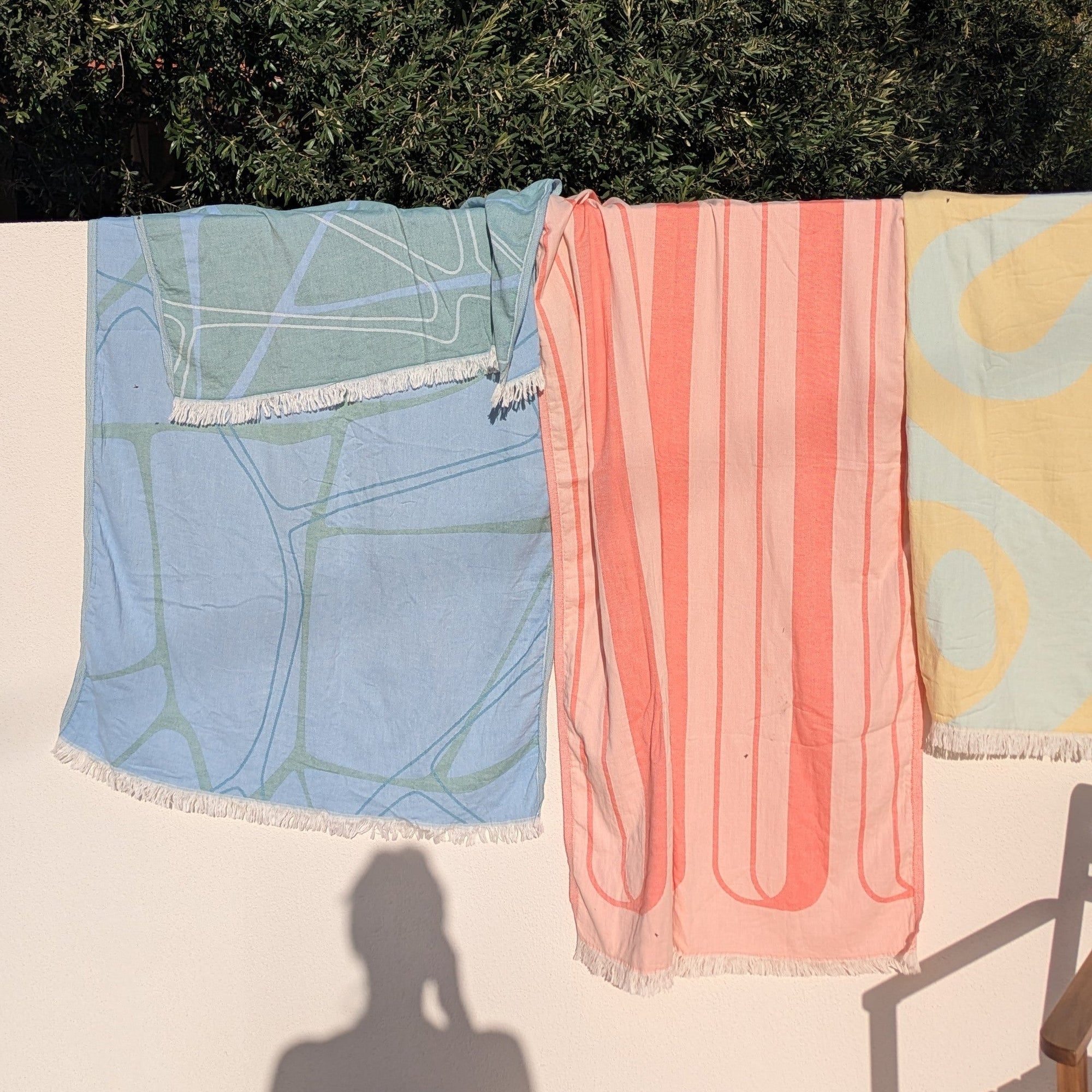 Two towels, one blue and one pink with a pattern, hanging on a line against a wall with trees in the background.
