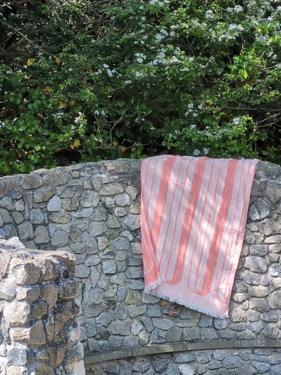 Laes Bridge Turkish Towel - Beach Towel - coral and blush - drying over a stone wall in the dappled light of leaves - shop now