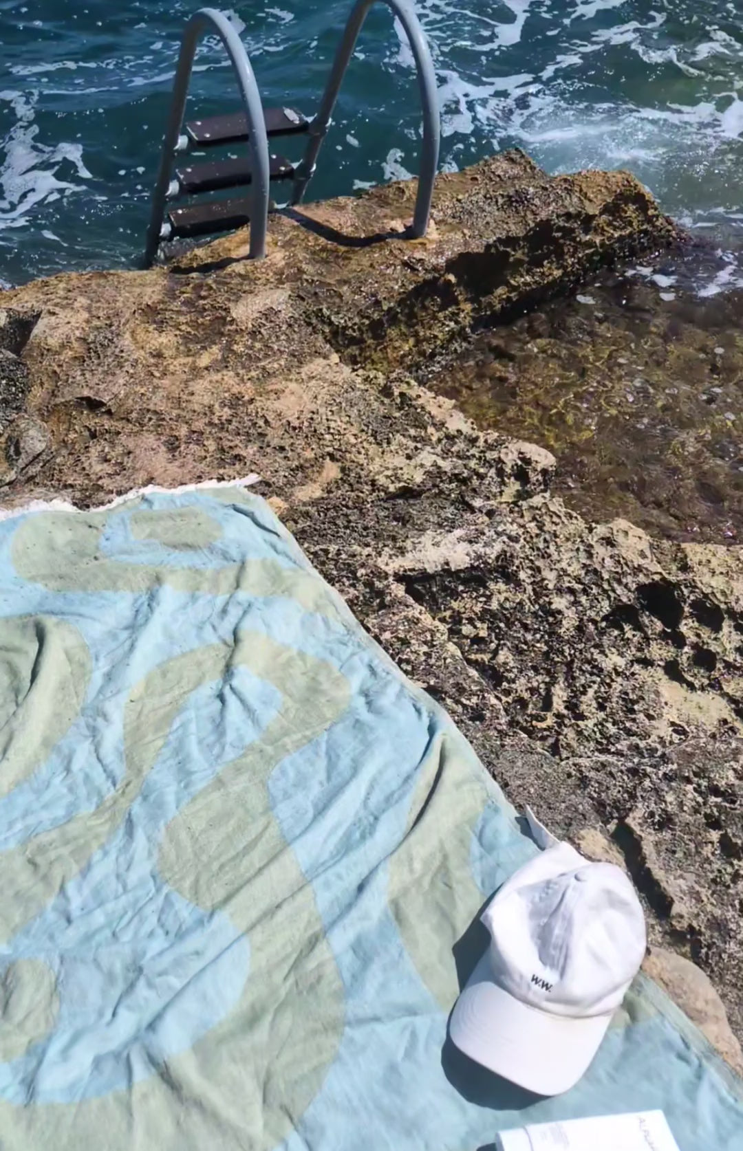 Laes Harbour Turkish Towel - Beach Towel - green/blue - white cap on a colorful towel on the rocks by the sea - shop now